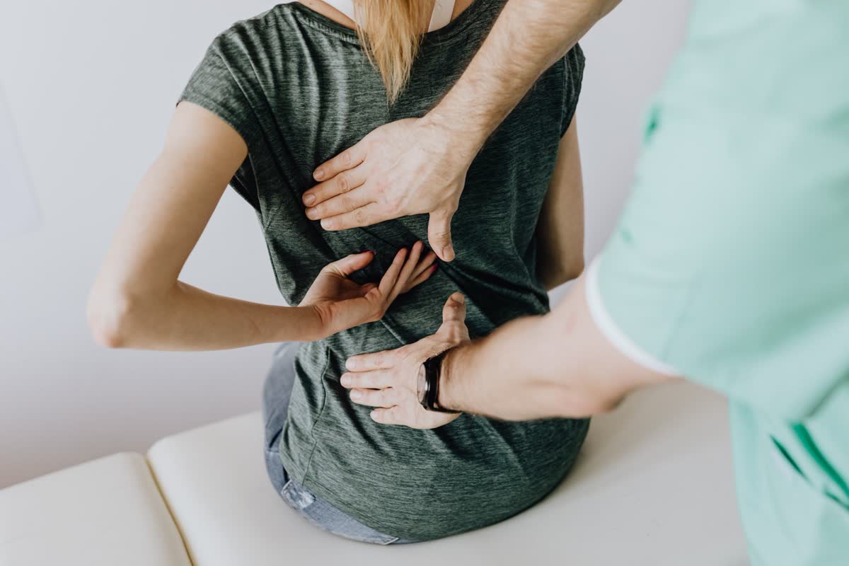 Close-up of a chiropractor's hands examining a patient's back in a bright treatment room