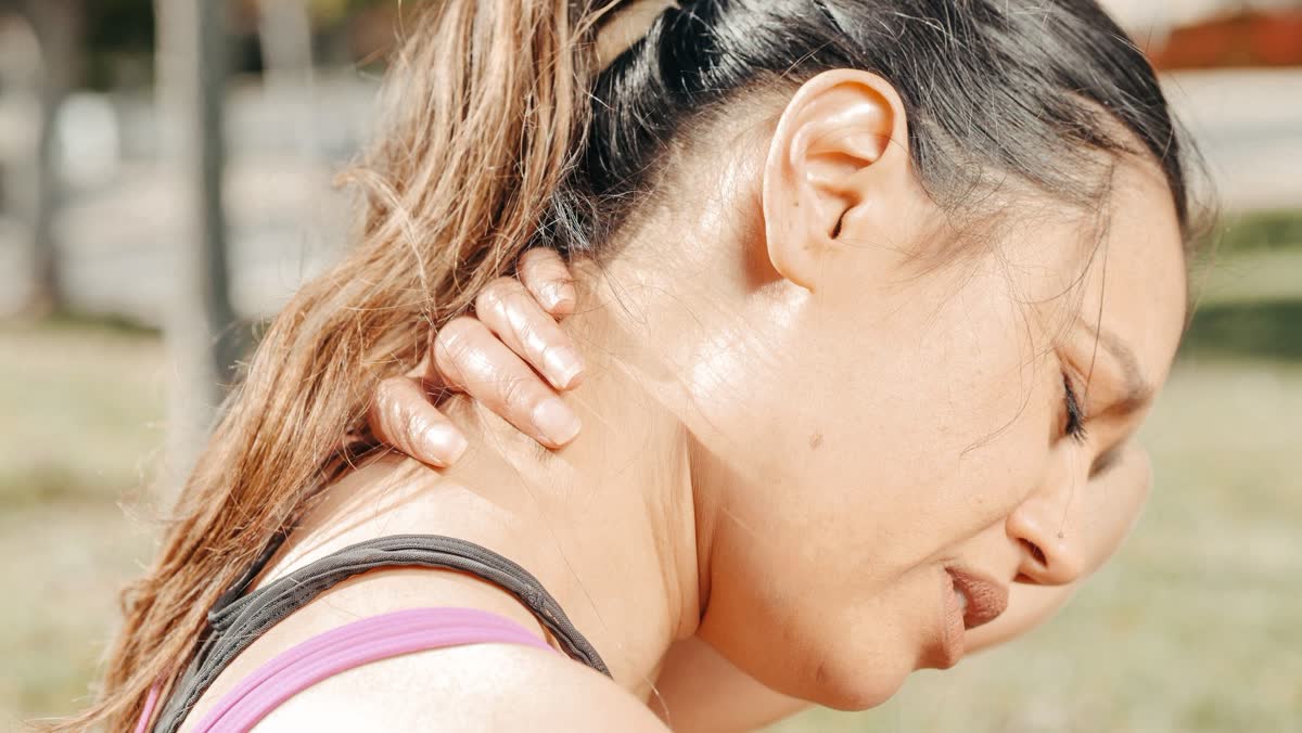 Woman with a hand on the back of her neck outdoors, feeling stiffness that appeared days after a crash