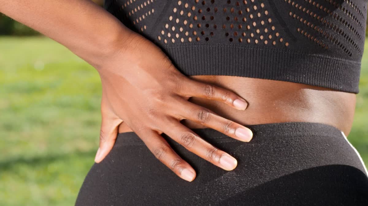 Close-up of a woman's hand resting on her lower back, showing low-back pain after a car accident