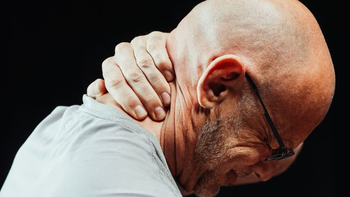 Man with his hand clamped on the back of his neck, showing tight muscles after an injury