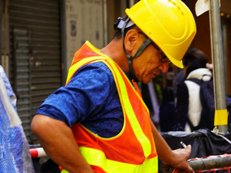 Worker in a hard hat and safety vest holding his lower back